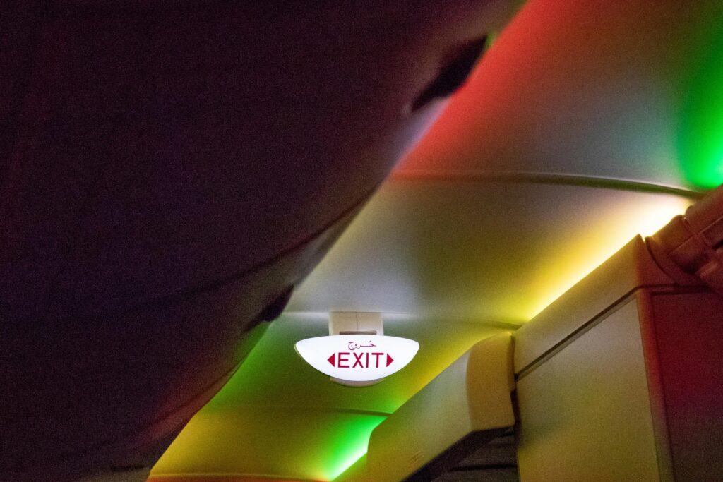 A vibrant exit sign inside an airplane cabin highlighted by colorful lighting.