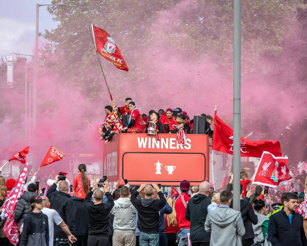 Celebratory parade in Liverpool with jubilant fans and players on an open-top bus.