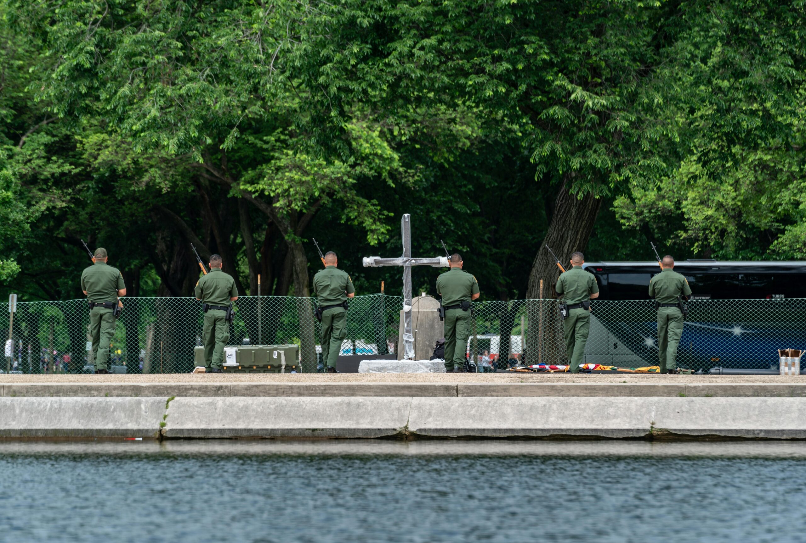 Military personnel participate in a solemn ceremony near a cross monument in Washington D.C. park.