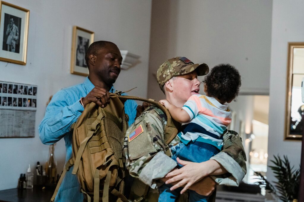 A soldier in uniform holds their child while their partner helps with packing.